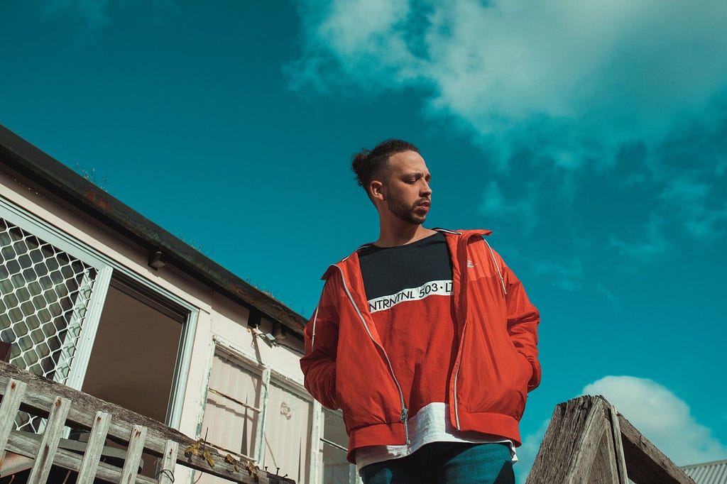 Flewnt wears a red jacket, looking away. Behind him is a clear, blue sky.