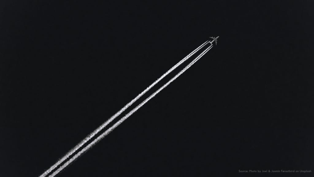 An airplane crossing a dark sky painting two white trails behind it.