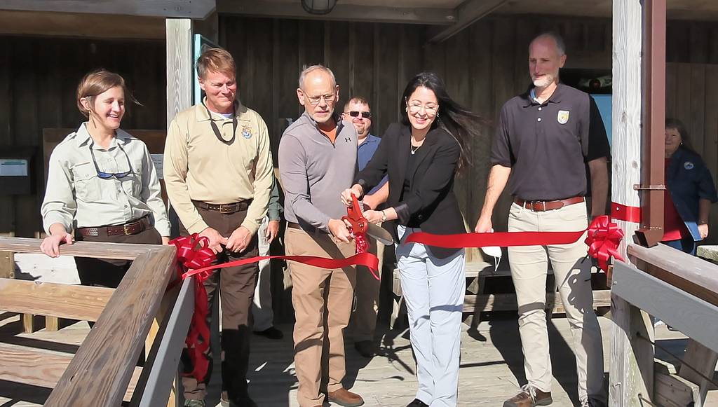 6 people behind red ribbon; one cuts ribbon