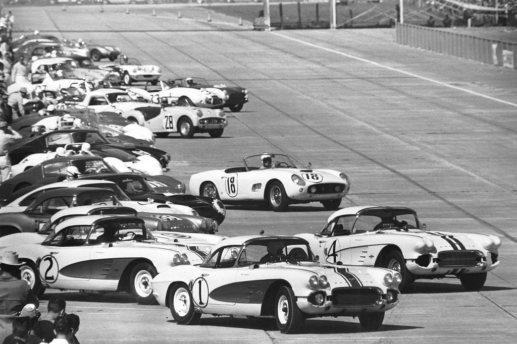 a black-and-white photo of antique racing cars lined up to start on a racecourse