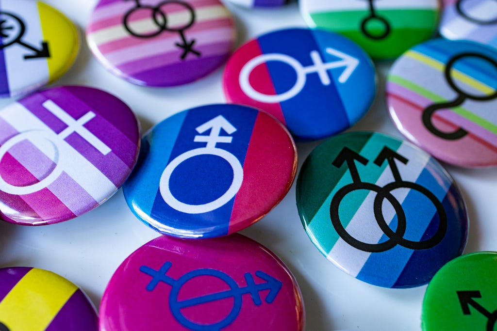 collection of button pins that have various gender symbols and colors