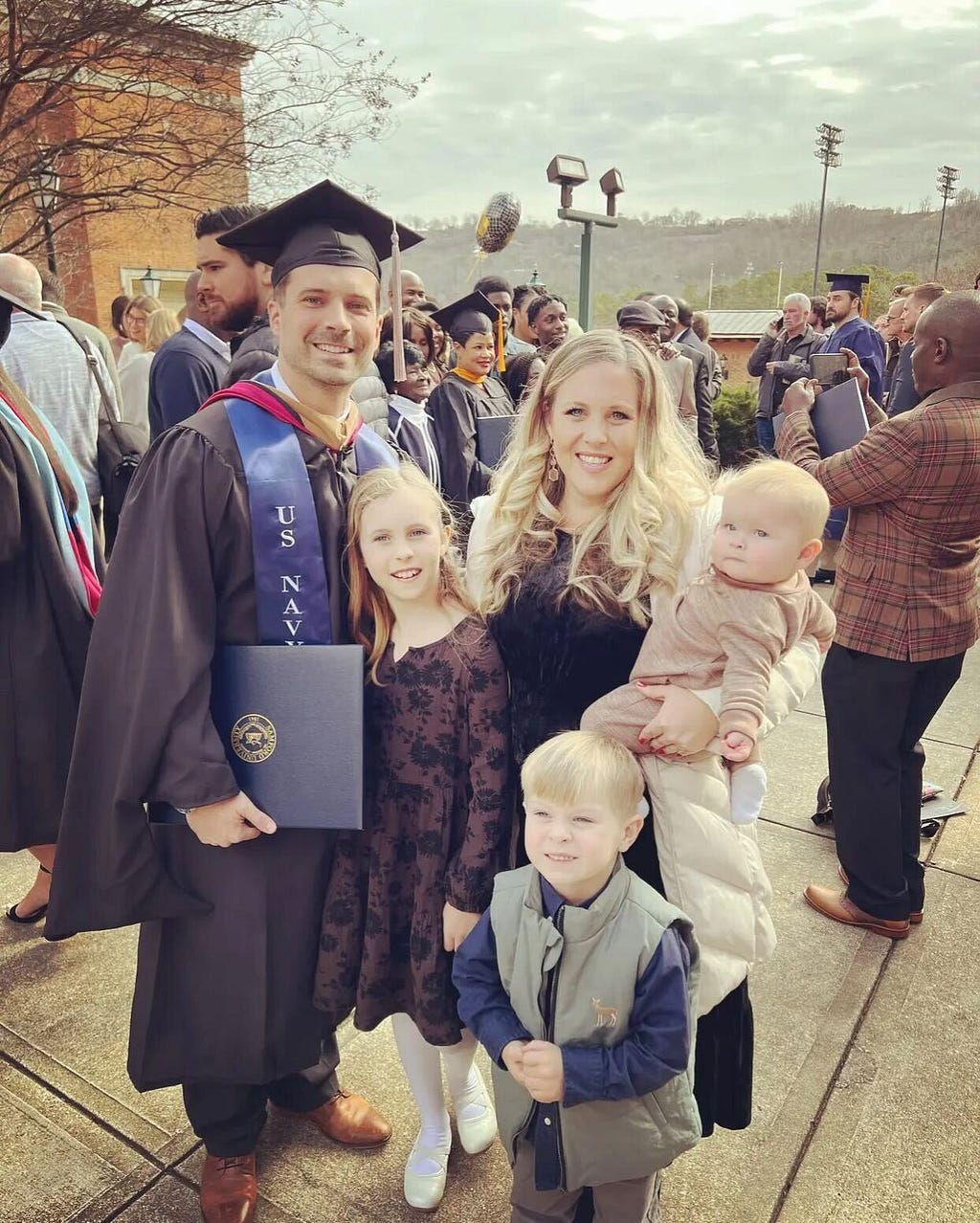 A man, his wife, and three children posing for a picture after a graduation ceremony outside of Pete Hannah Center at Samford University.