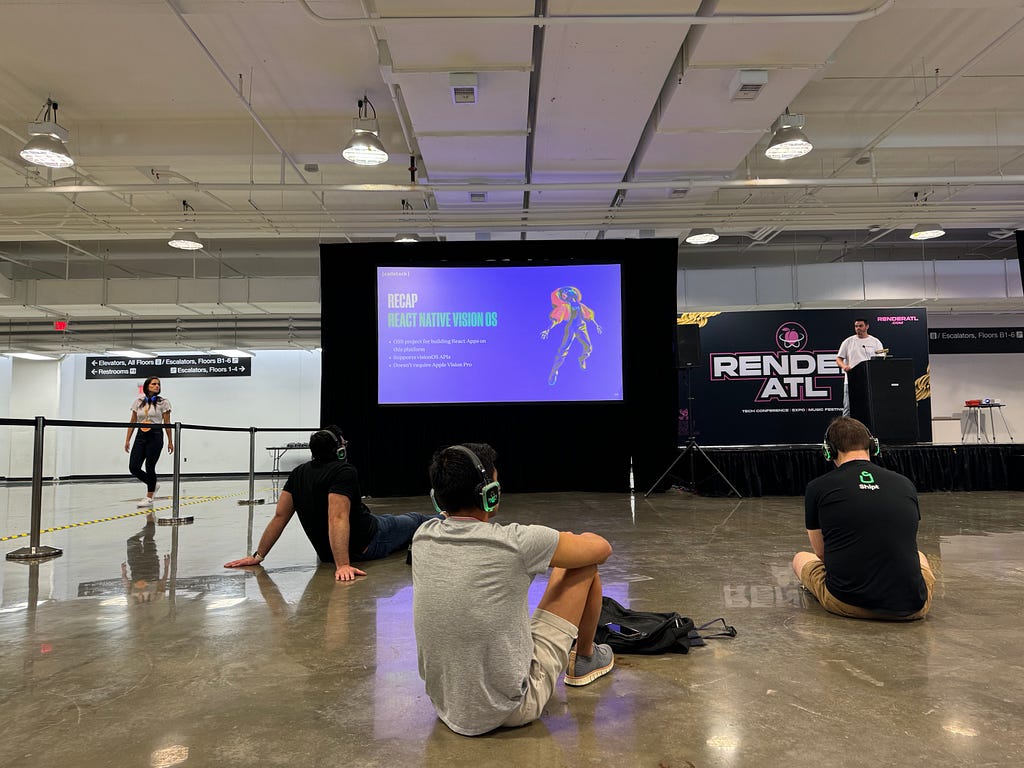 Three people with headphones on watching a presentation while sitting on the floor.