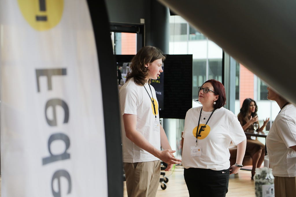 In the foreground on the left is a Federation Community flag. In the background, three event makers are conversing. They are wearing white t-shirts with Federation branding.