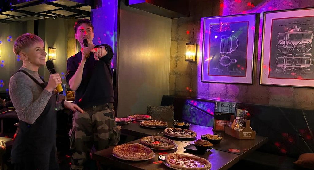 Mitchell and another student smiling and performing at a karaoke and pizza event in a bar.