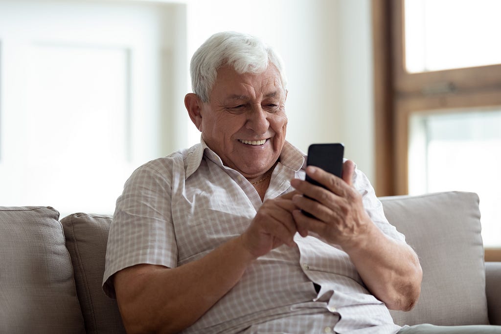 Older man smiles while reading off a cell phone screen.