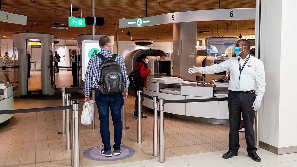 An airport security officer directs a passenger forward at Schiphol Airport.