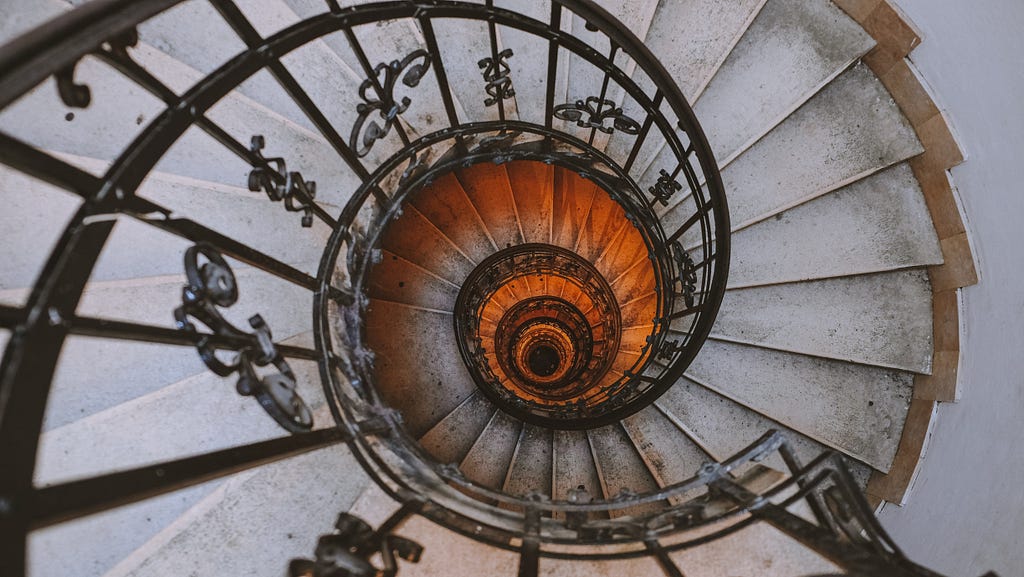 A spiral staircase leading down. Photo is taken so you can see the spiral descending into darkness.