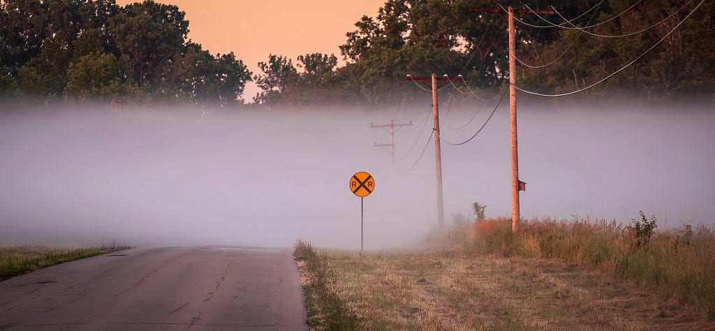 Fog over a country road at sunrise with a railroad crossing sign