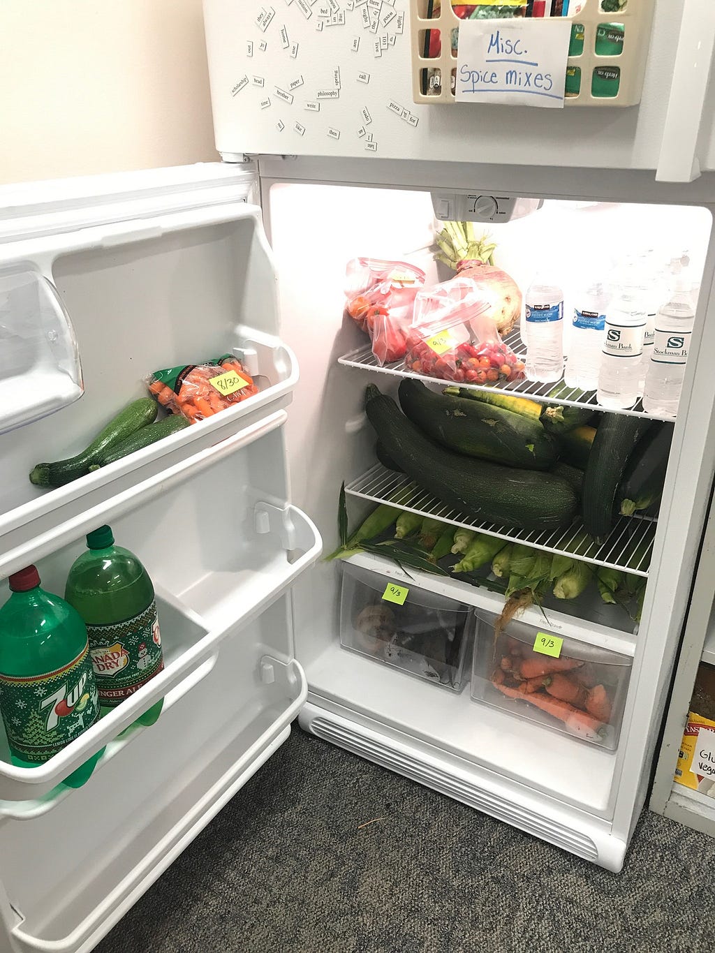 Picture of a refrigerator full of vegetables and bottles of water.