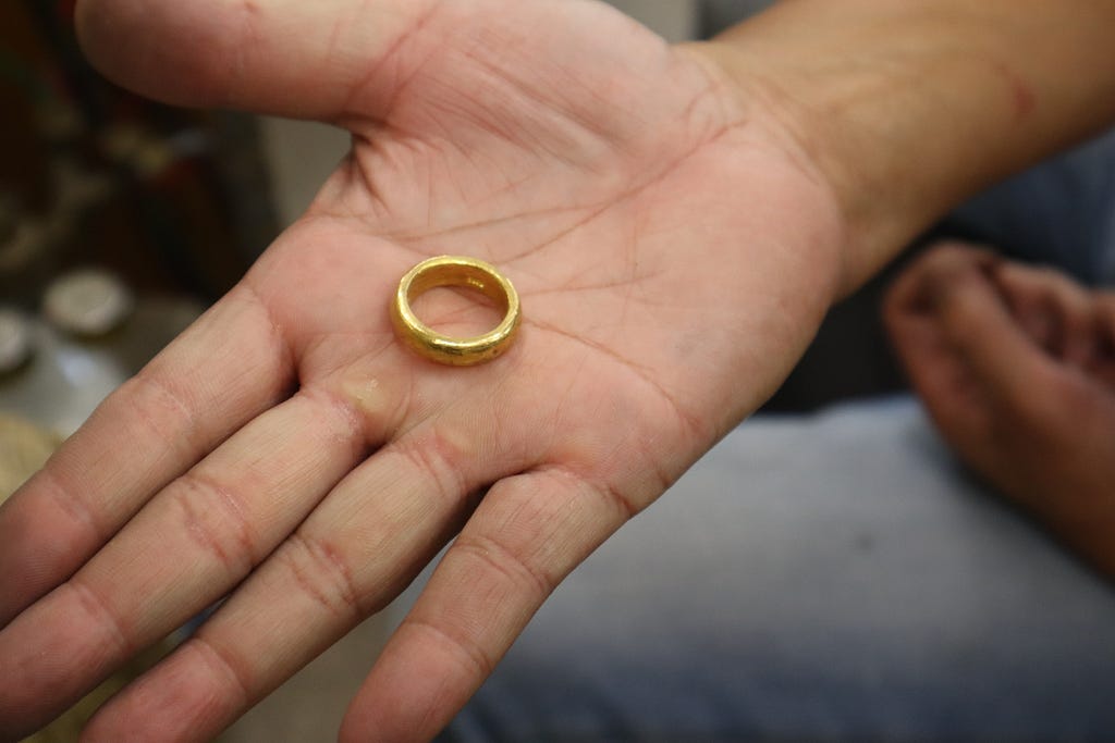 A simple gold band is centered in the middle of Phillip’s open right palm. His hand takes up most of the frame. In the bottom right, out of focus, the viewer can see the faded blue jeans of his lap, his left hand resting on his leg.