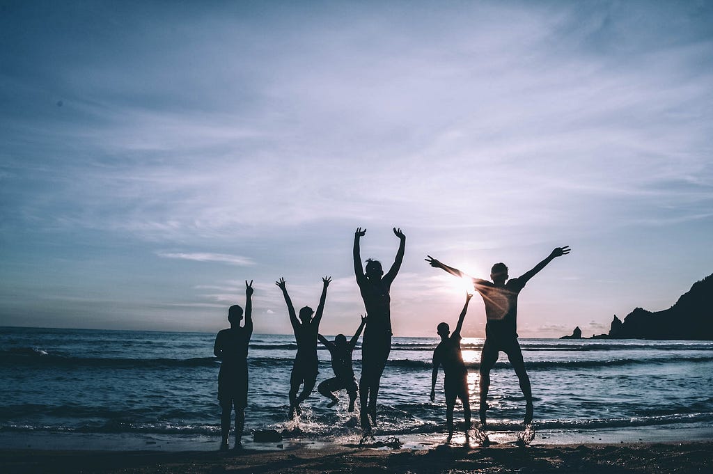 A group of people jumping for joy at the beach during sunset.