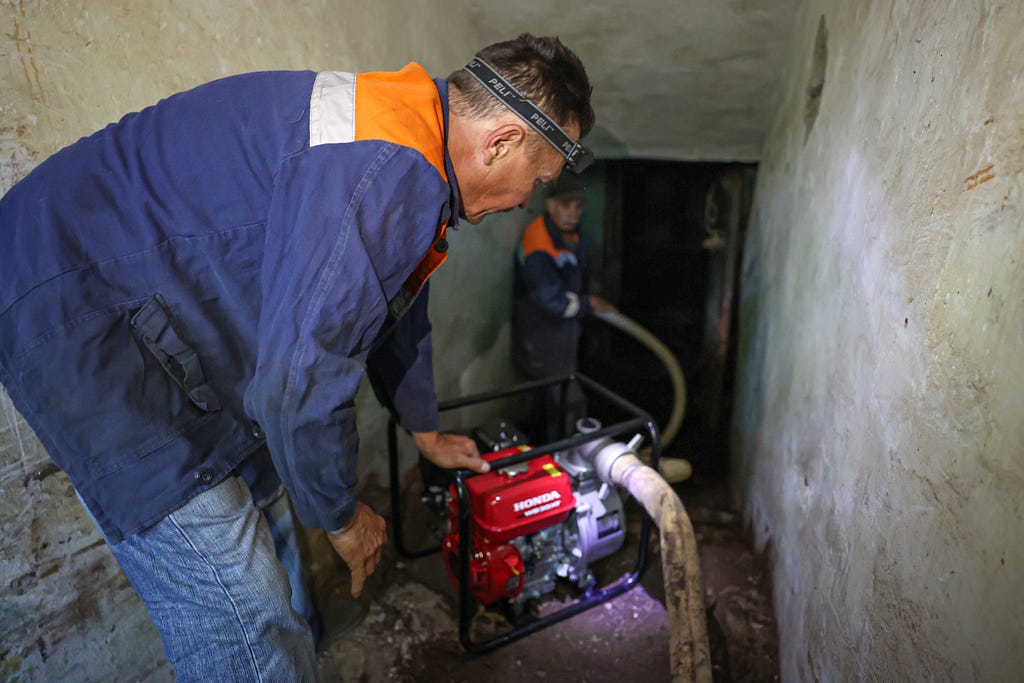 A man leans over a machine that pumps water out of flooded buildings.