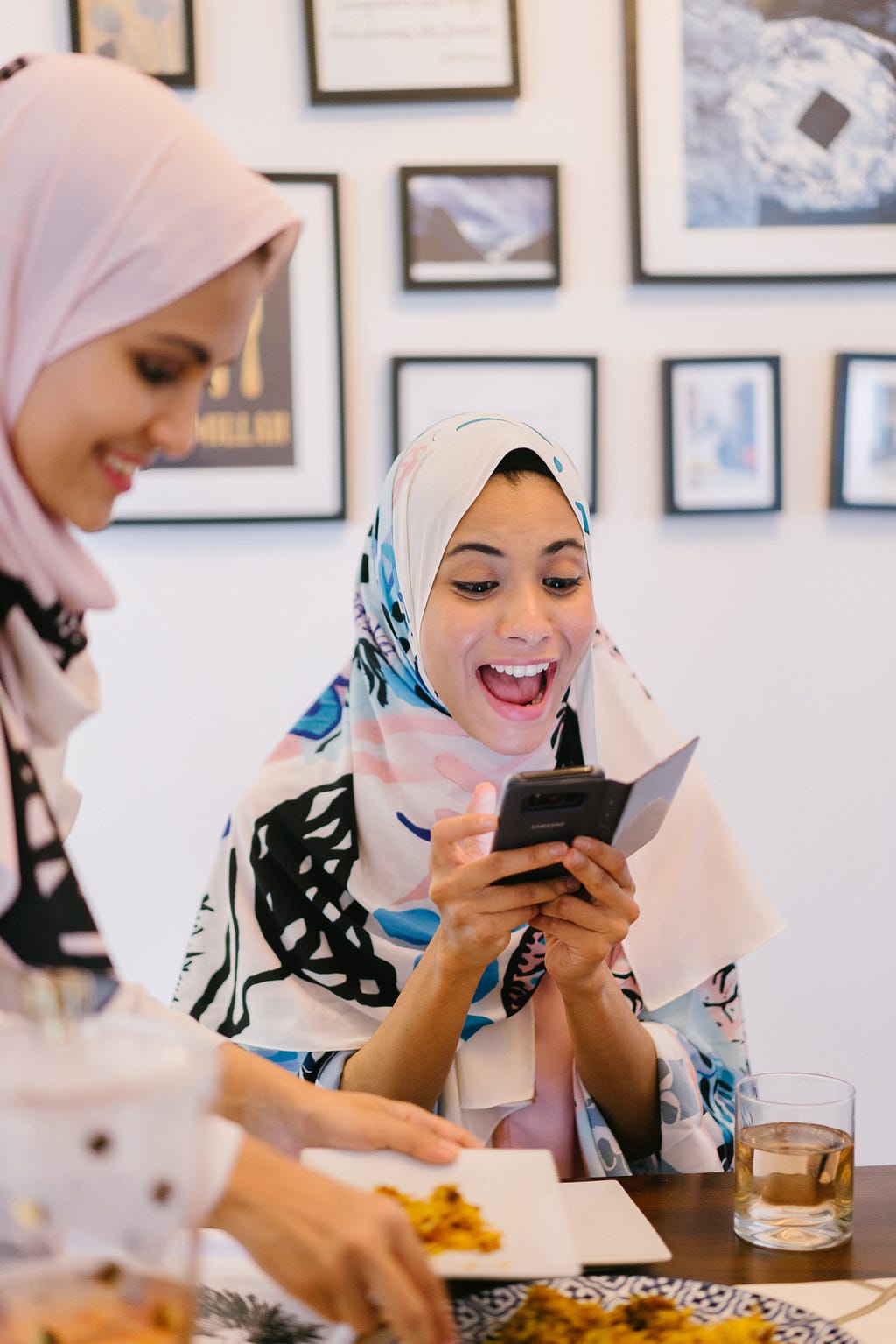 A young woman wearing a hijab holding her phone close to her face smiles in exitement.