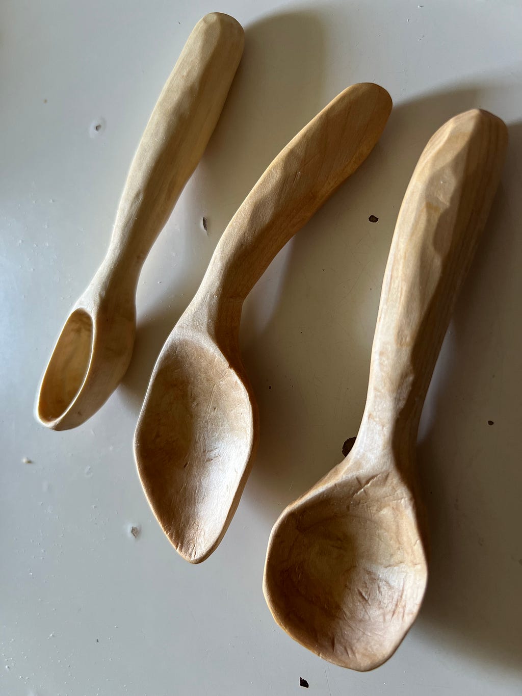 Three small, handcarved wooden spoons on a white tabletop.