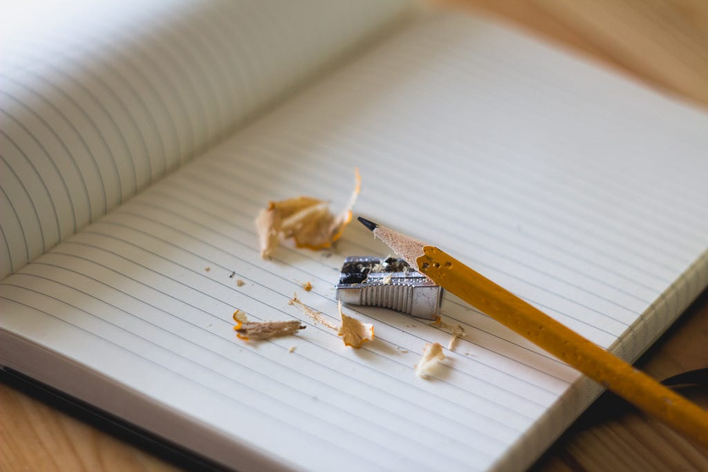 A pencil on top of a notebook with a pencil sharpener and pencil shavings