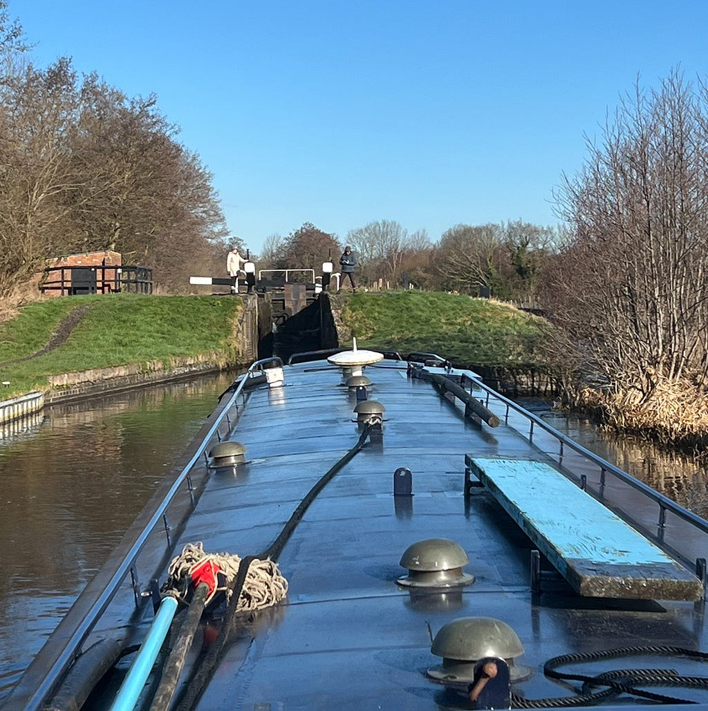Narrowboat approaching lock with the crew onshore turning the lock.