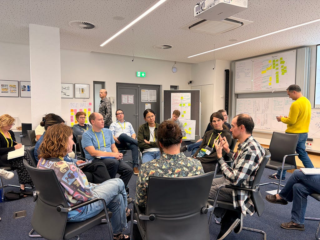 A circle of seven folks from industry, surrounded by a larger circle of academics listening.
