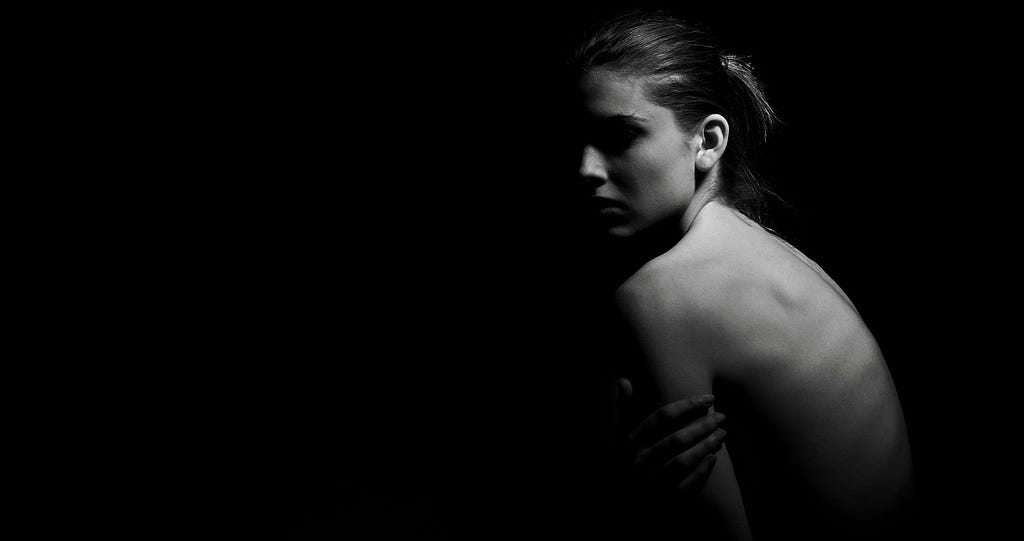 Black & white photo of young woman, obscured face, bare back turned to the camera