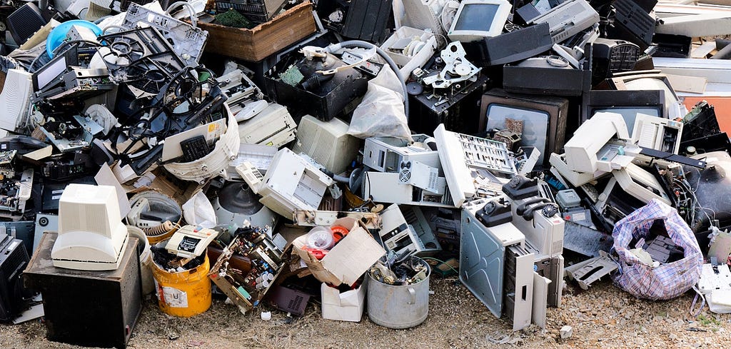 A large pile of discarded electronic gadgets on a waste dump including computers and tvs