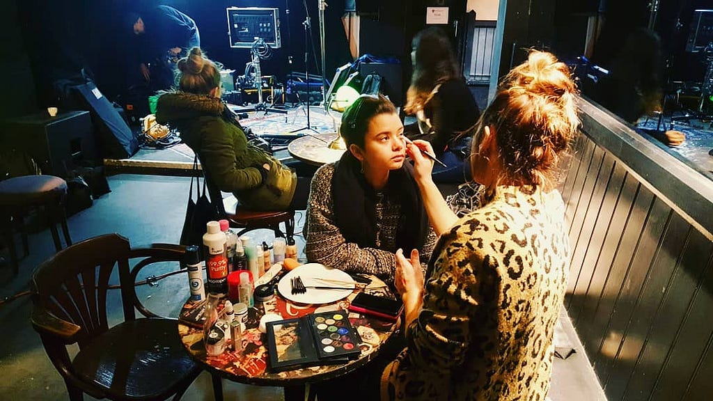 a behind the scenes shot of a movie set, an actor is getting makeup applied