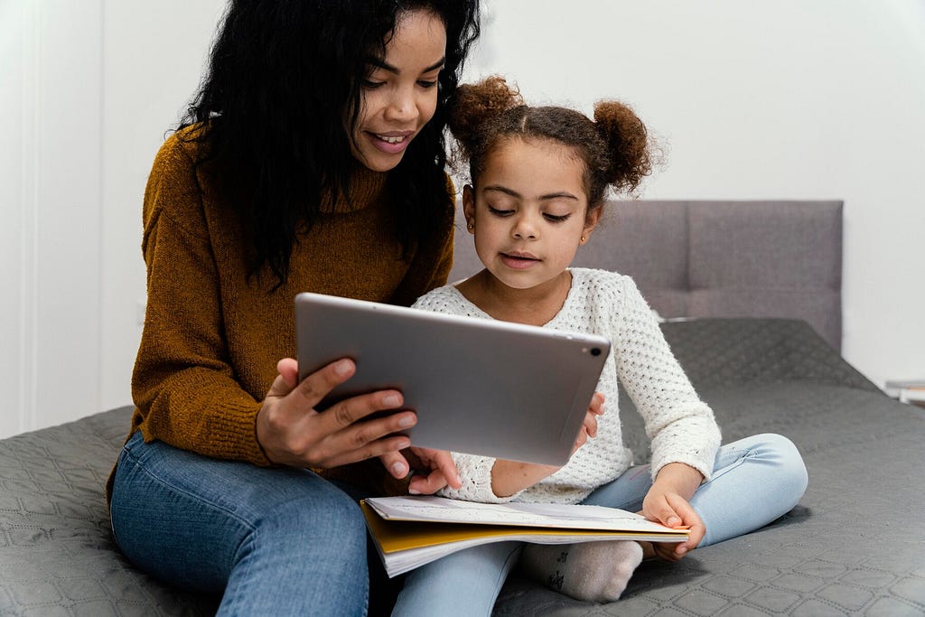 A mother and her child learning with a book and a tablet