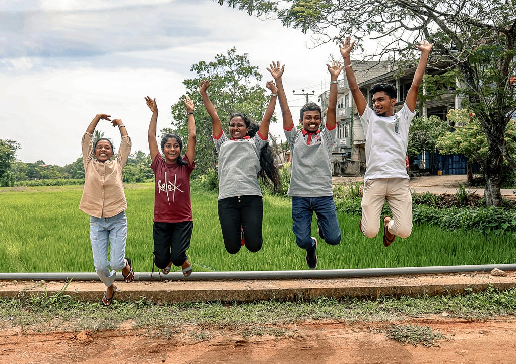 Five young adults leap into the air in unison with their arms reaching to the sky.