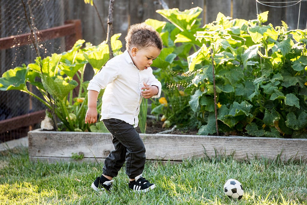 young toddler kicks a soccer ball on the grass