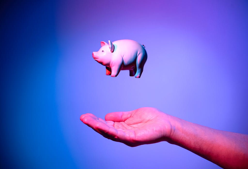 A pink piggy bank in mid-air above someone’s hand.