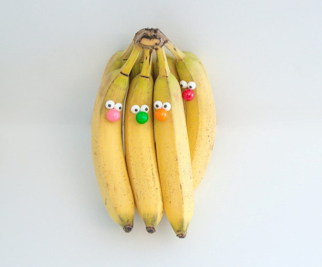 A bunch of bananas wearing googly eyes and colorful clown noses.