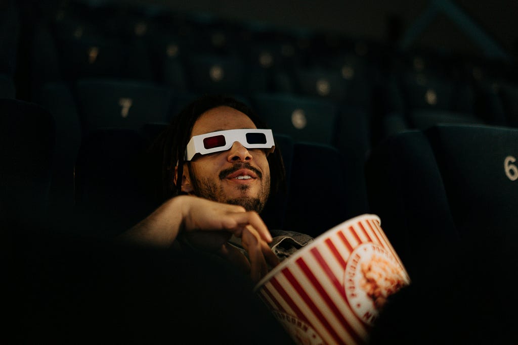 A man with a bowl of popcorn seeing a movie at a cinema