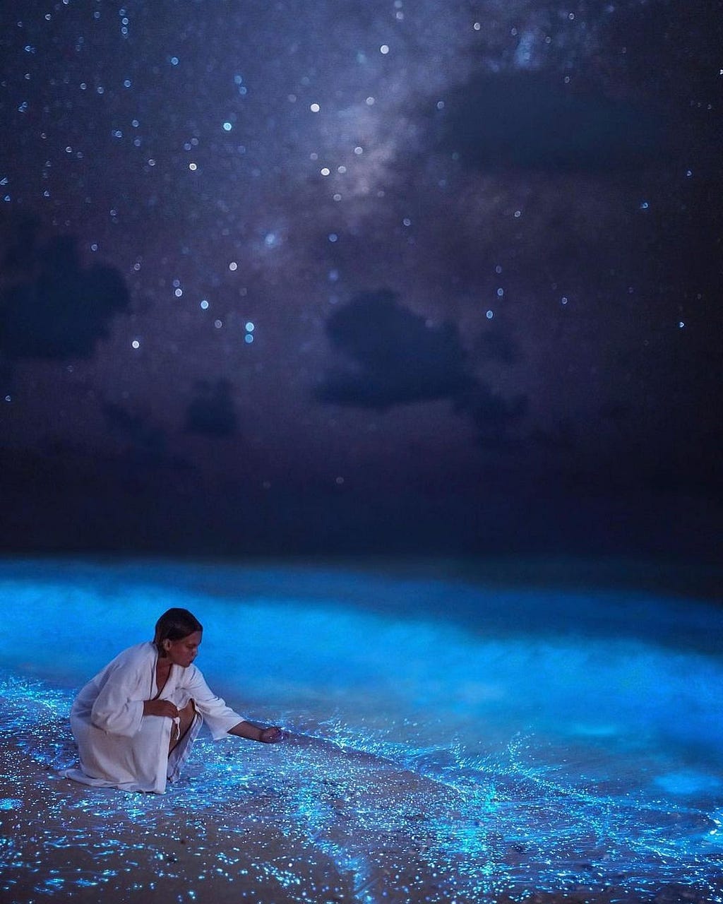 A woman scooping bioluminescent plankton with her hand at nighttime in the Maldives.