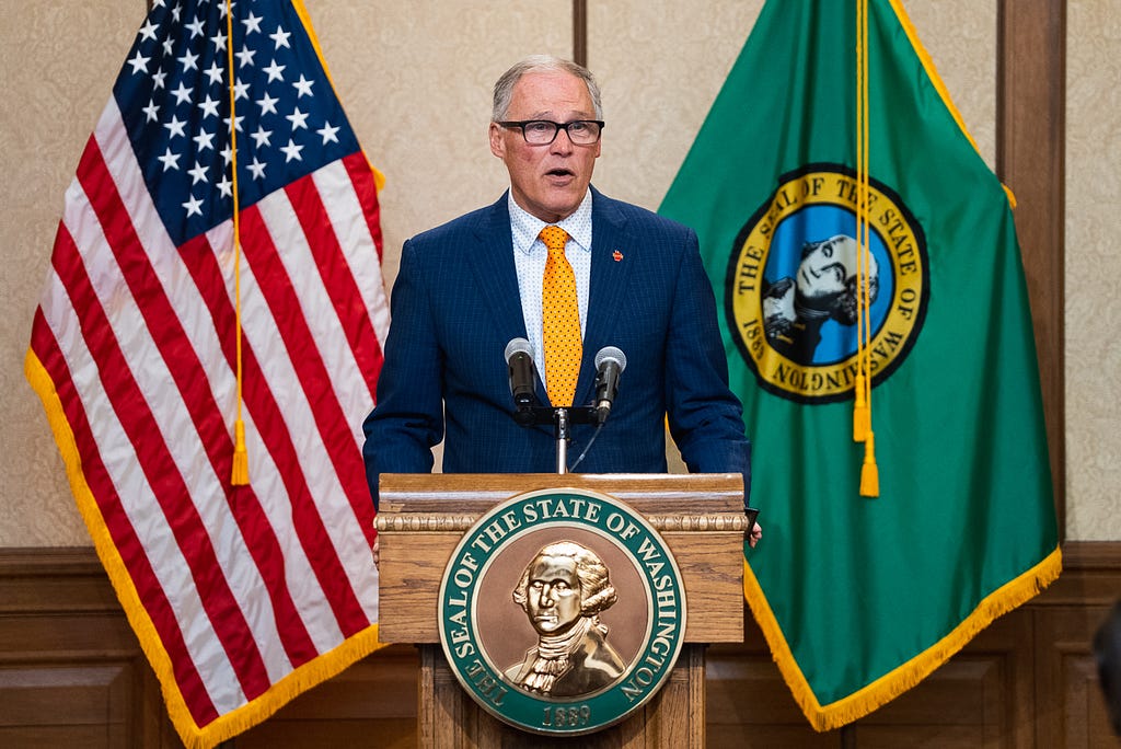 Gov. Inslee standing at a podium with flags on either side