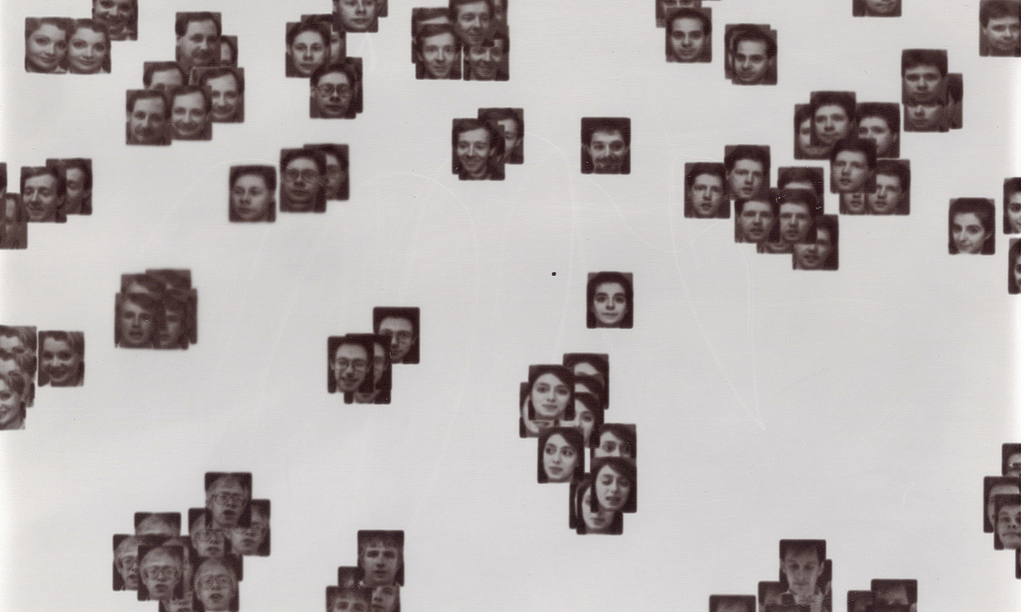 A laptopogram based on a neutral background and populated by scattered squared portraits, all monochromatic, grouped according to similarity. The groupings vary in size, ranging from single faces to overlapping collections of up to twelve. The facial expressions of all the individuals featured are neutral, represented through a mixture of ages and genders.