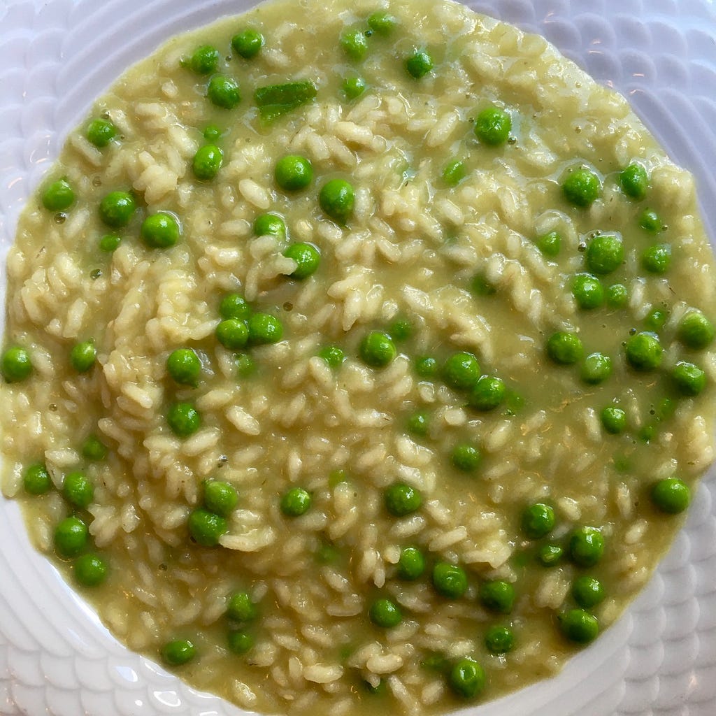 Overhead view of a bowl of yellowish-brownish risotto with peas in it.