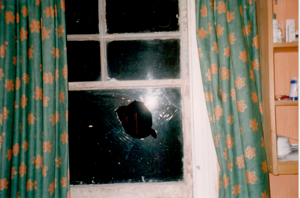 A broken window pane. There is a large hole in the window surrounded by cracks in the shatter-proof glass.