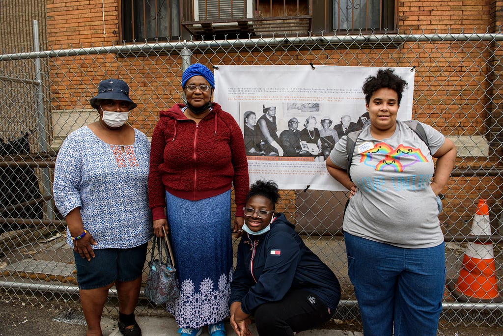 A group of women pose in front of a criminal justice system advocacy banner, hanging on a fence