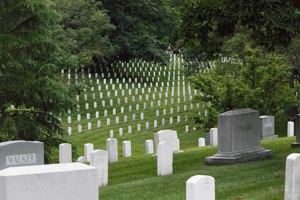 Aerial view of a cemetery with rows of white headstones on a green hillside surrounded by dense trees