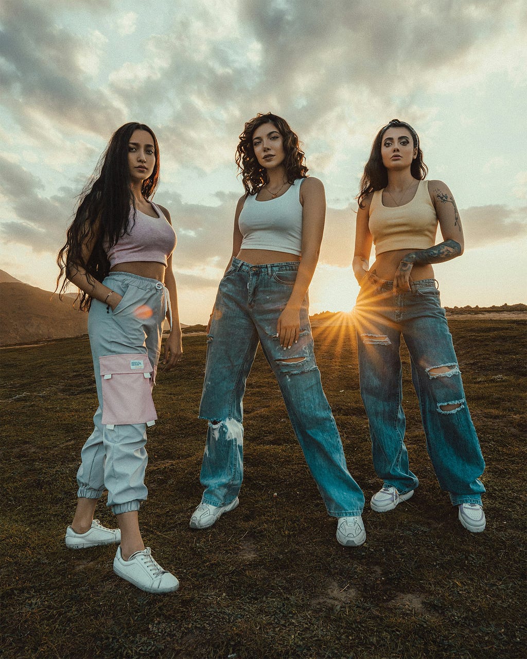 3 young ladies on a field, 2 with a cropped sports top and flared jeans on