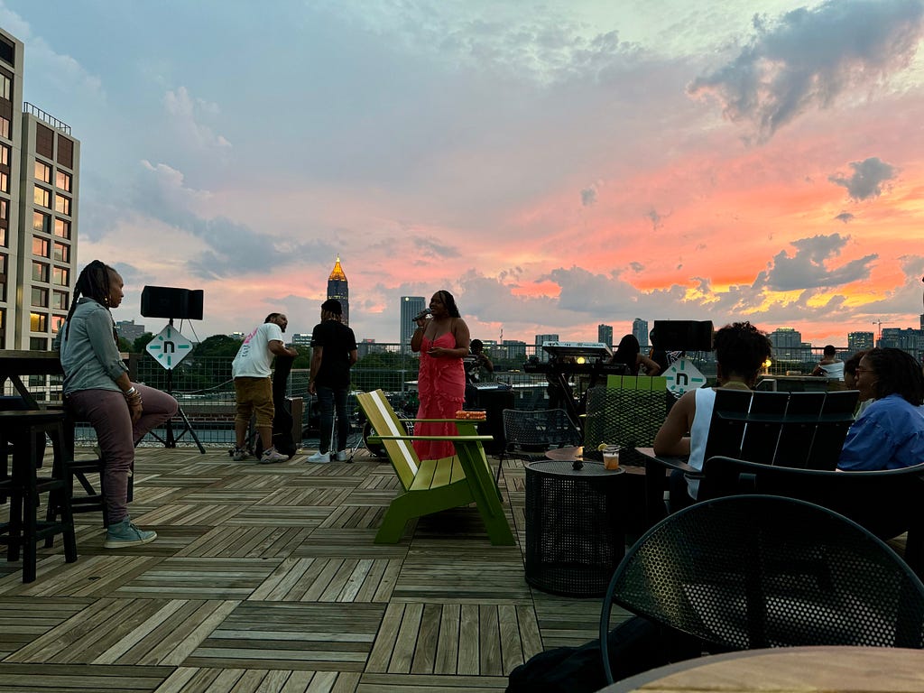 Render ATL hosts a rooftop event with organizers welcoming guests with an R&B band in front of a bright orange sunset.