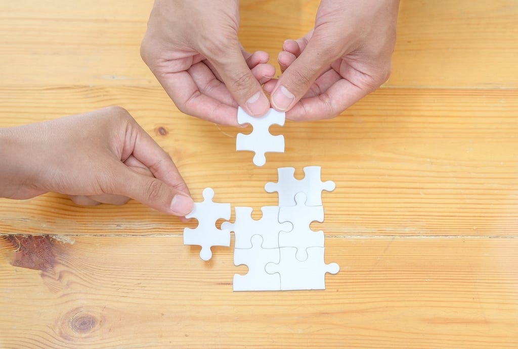 An image of two people’s hands working on a puzzle.