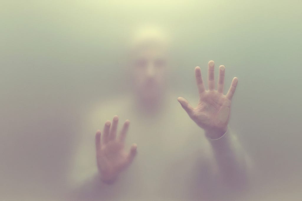 Two hands pressed against a translucent barrier from inside, palms open, depicting confinement in a self-built prison.