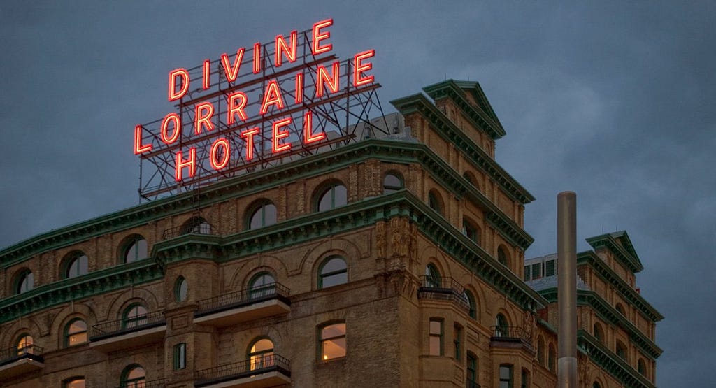 A photograph of a large 19th-century hotel with the words “Divine Lorraine Hotel” illuminated in a neon sign on its roof.