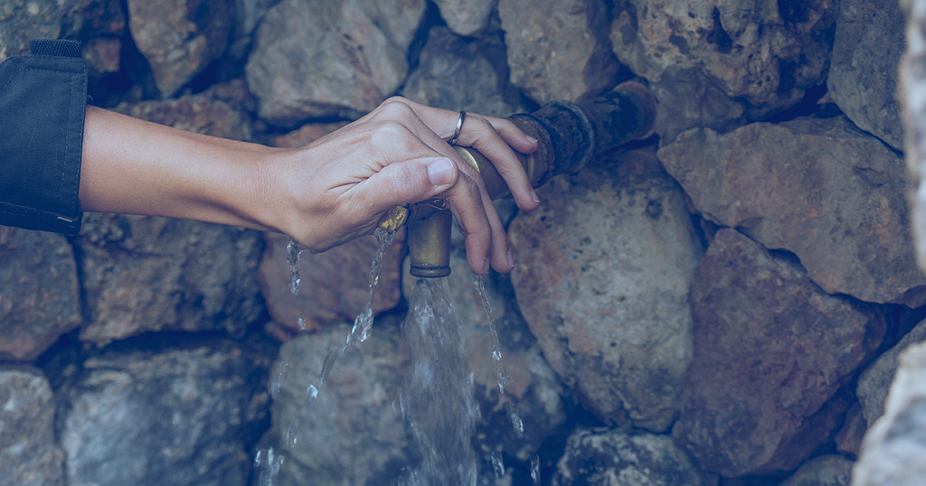 Picture showing a woman's hand opening a tap coming out of a stone wall.