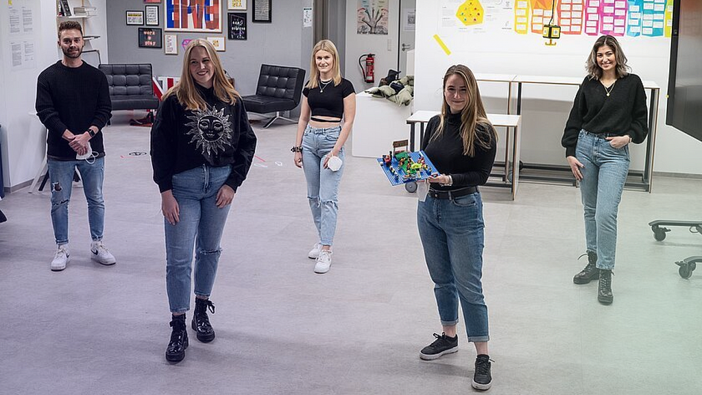 The five winning students from the University of Neu-Ulm stand in a large, open classroom space displaying their winning sustainable UX concept