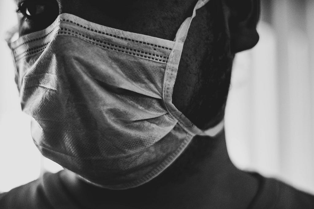 A black man looking off to the left and wearing a face mask.