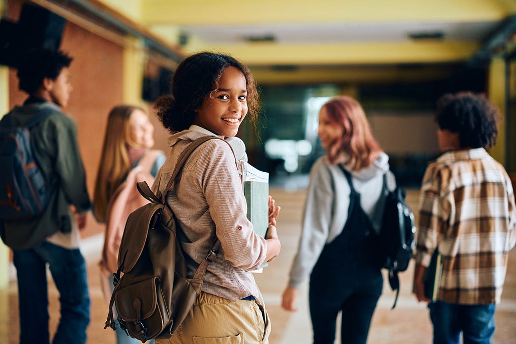 One girl student looking back with four students walking ahead in a school hallway.