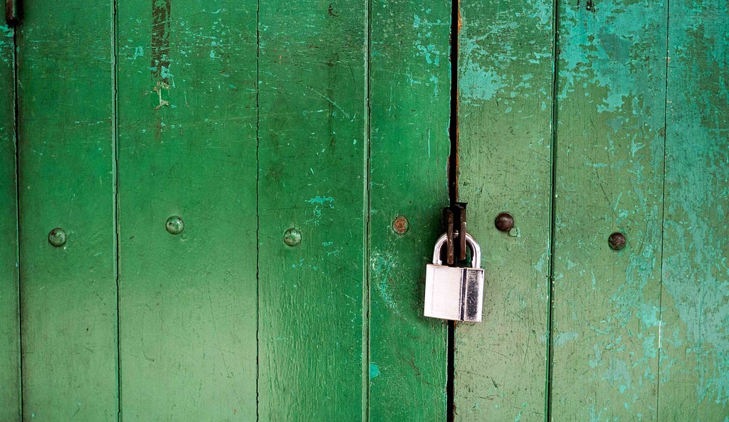 A green gate, closed with a padlock.