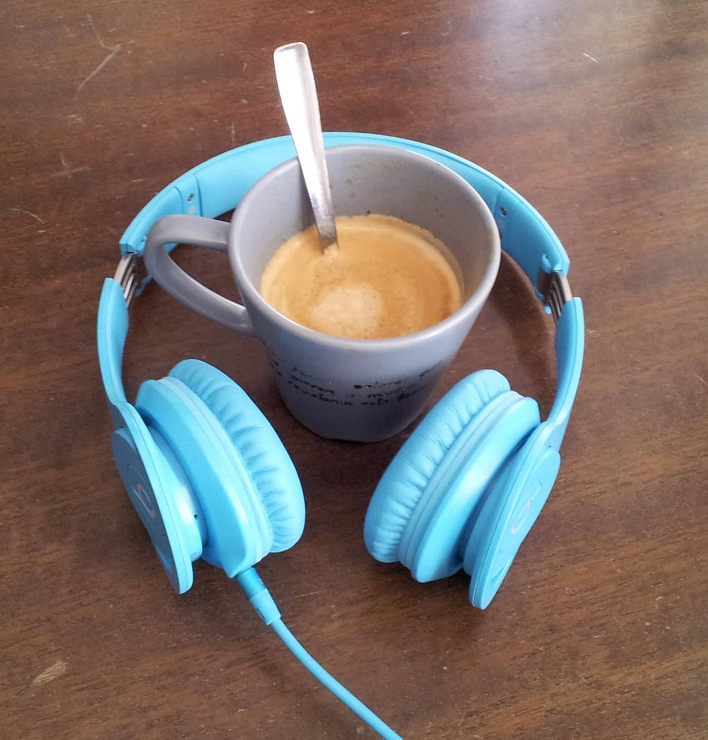 Blue on-ear headphones circling a cup of coffee on a brown wooden table