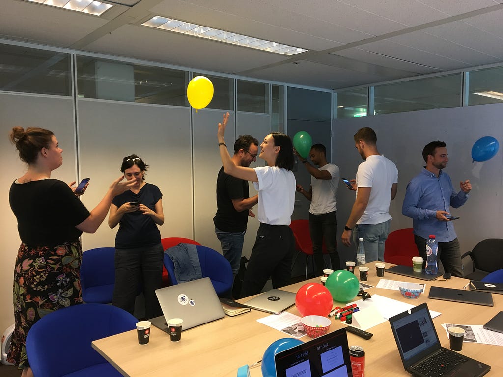 People in a room keeping a balloon in the air while performing a task on their mobile phones.